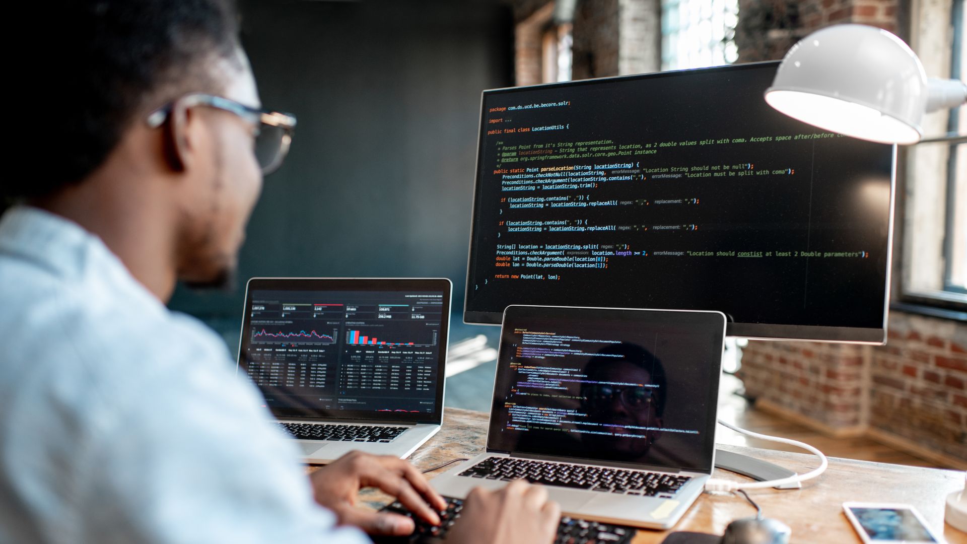 A man has three computer monitors in front of him. He's typing a series of codes